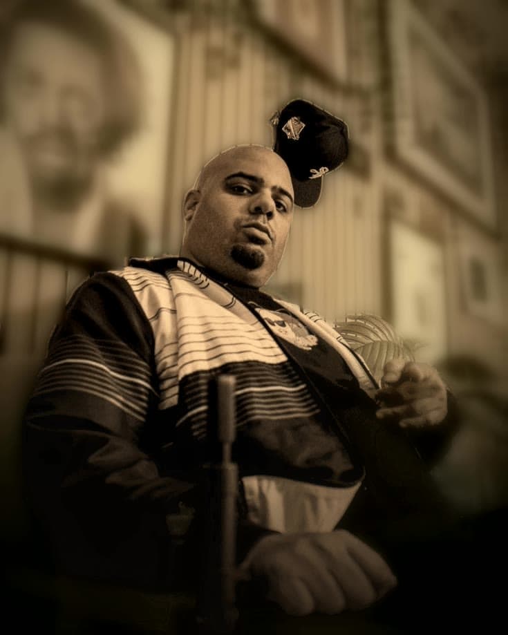Starvin Marv in his studio, seated in front of a wall of framed hip-hop prints